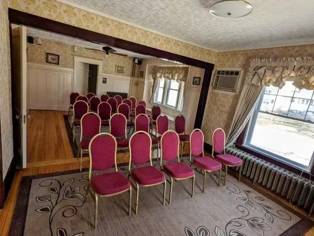 Small banquet room with rows of pink chairs facing the front and a window on the right.