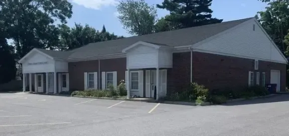 Single-story brick and white commercial building with a small portico and empty parking lot