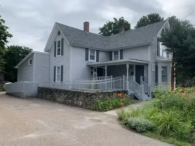 Gray two-story house with white trim, stone foundation, and front porch beside a driveway and garden.