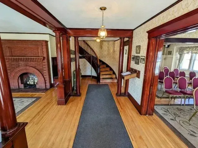 Historic room with wooden beams, staircase, fireplace, and carpet runner leading to a dining area