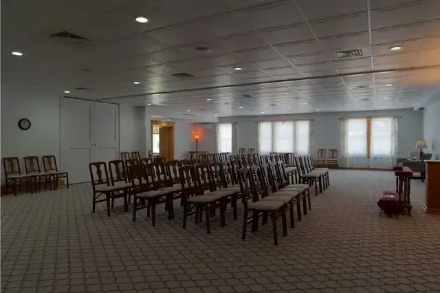 Empty banquet hall with rows of chairs facing a front stage and windows.