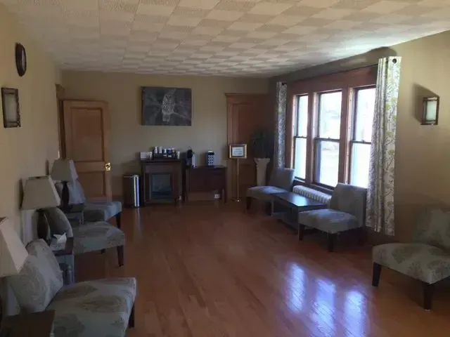 Empty living room with hardwood floors, a fireplace, chairs, and large windows letting in daylight