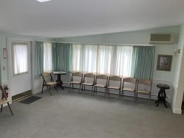 Empty waiting room with rows of chairs, large windows with curtains, and a carpeted floor.