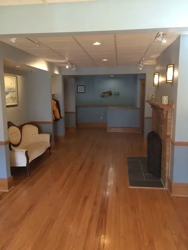 Empty living room with hardwood floors, fireplace, and white armchair under warm wall lights