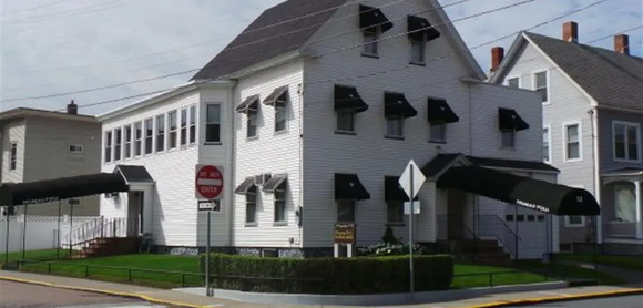 White two-story building on a street corner with black awnings and a stop sign nearby