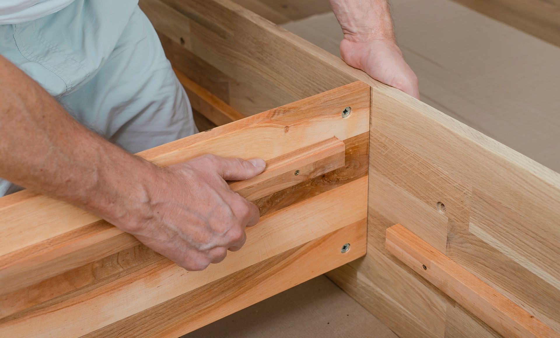 Hands assembling a wooden bed frame with a clamp in a workshop
