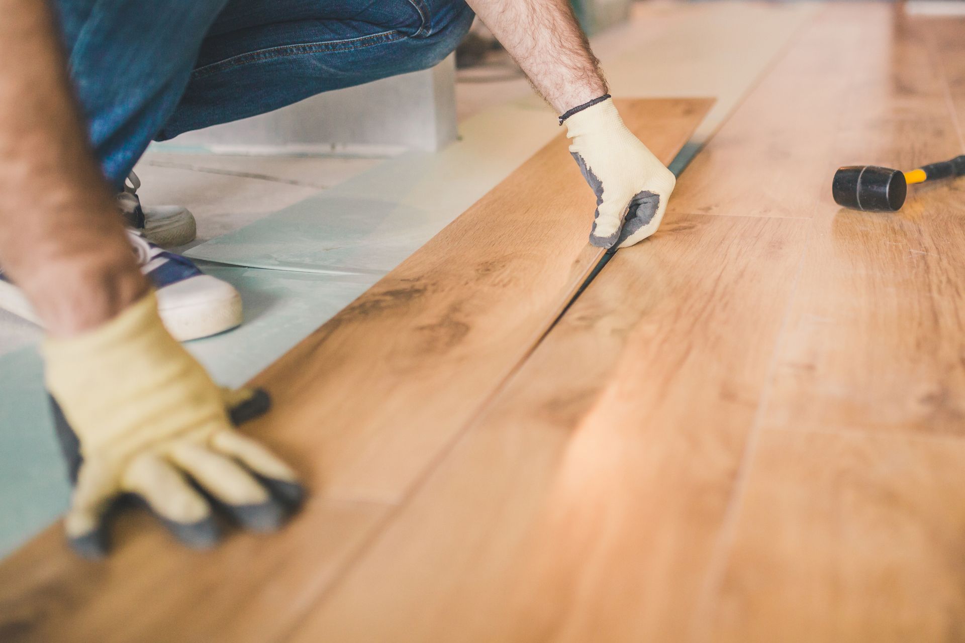 Person installing hardwood flooring with a tool and gloves in a room