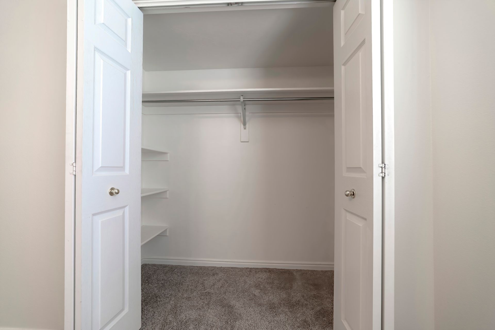 Open closet with white double doors, hanging rod, and carpeted floor