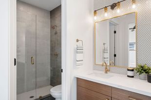 Modern bathroom with glass shower, mosaic tile, and vanity with gold-framed mirror and lights