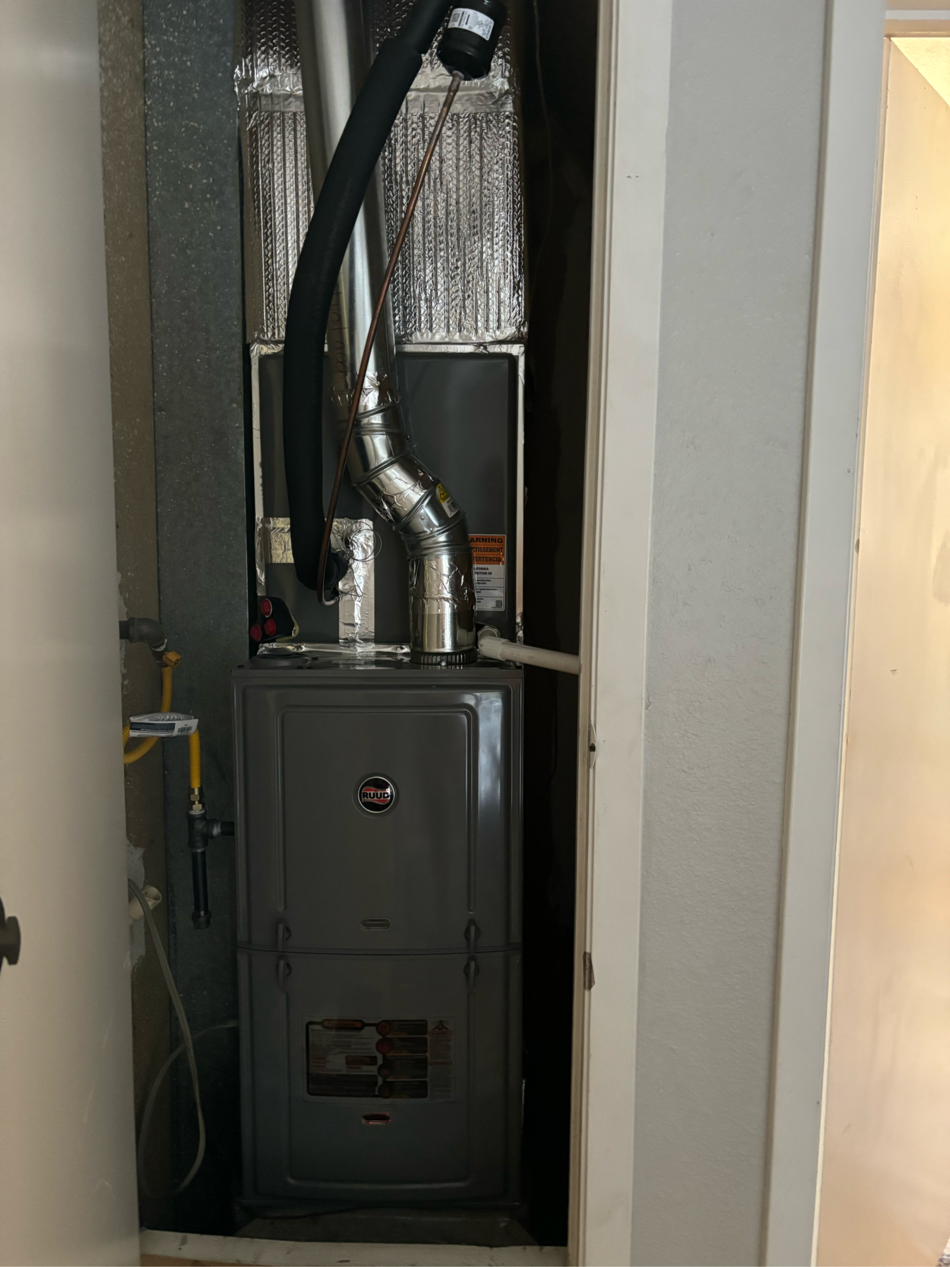 Gray furnace in a utility closet with vent and gas lines.