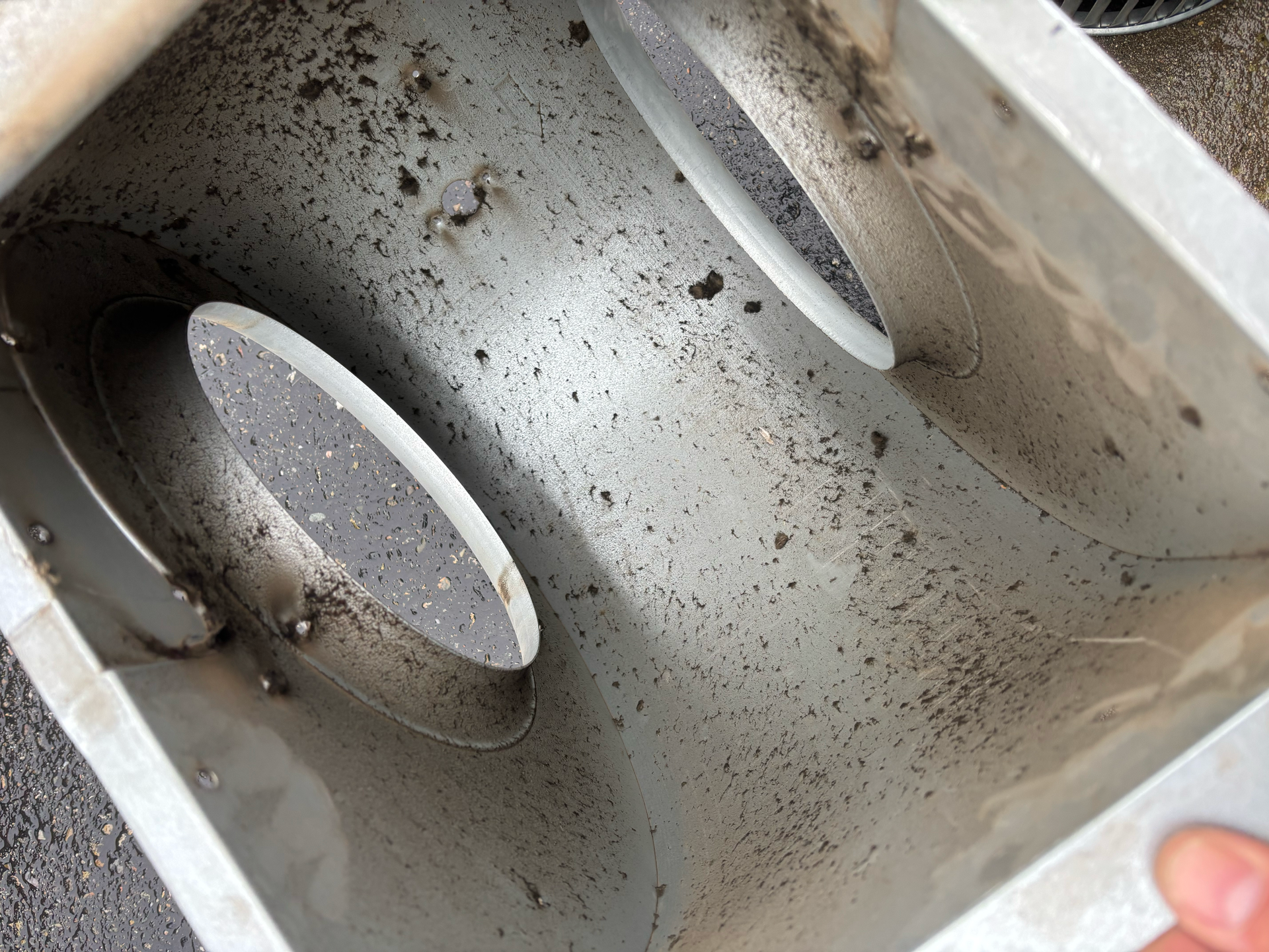 Inside of a metal container with two oval-shaped filters, covered in dirt and debris.