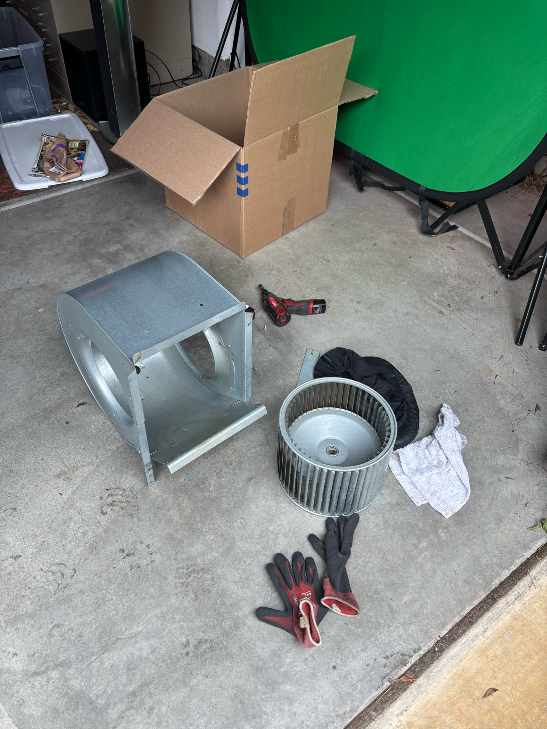 HVAC parts, including a blower wheel and housing, tools, and gloves, sit on concrete outside.