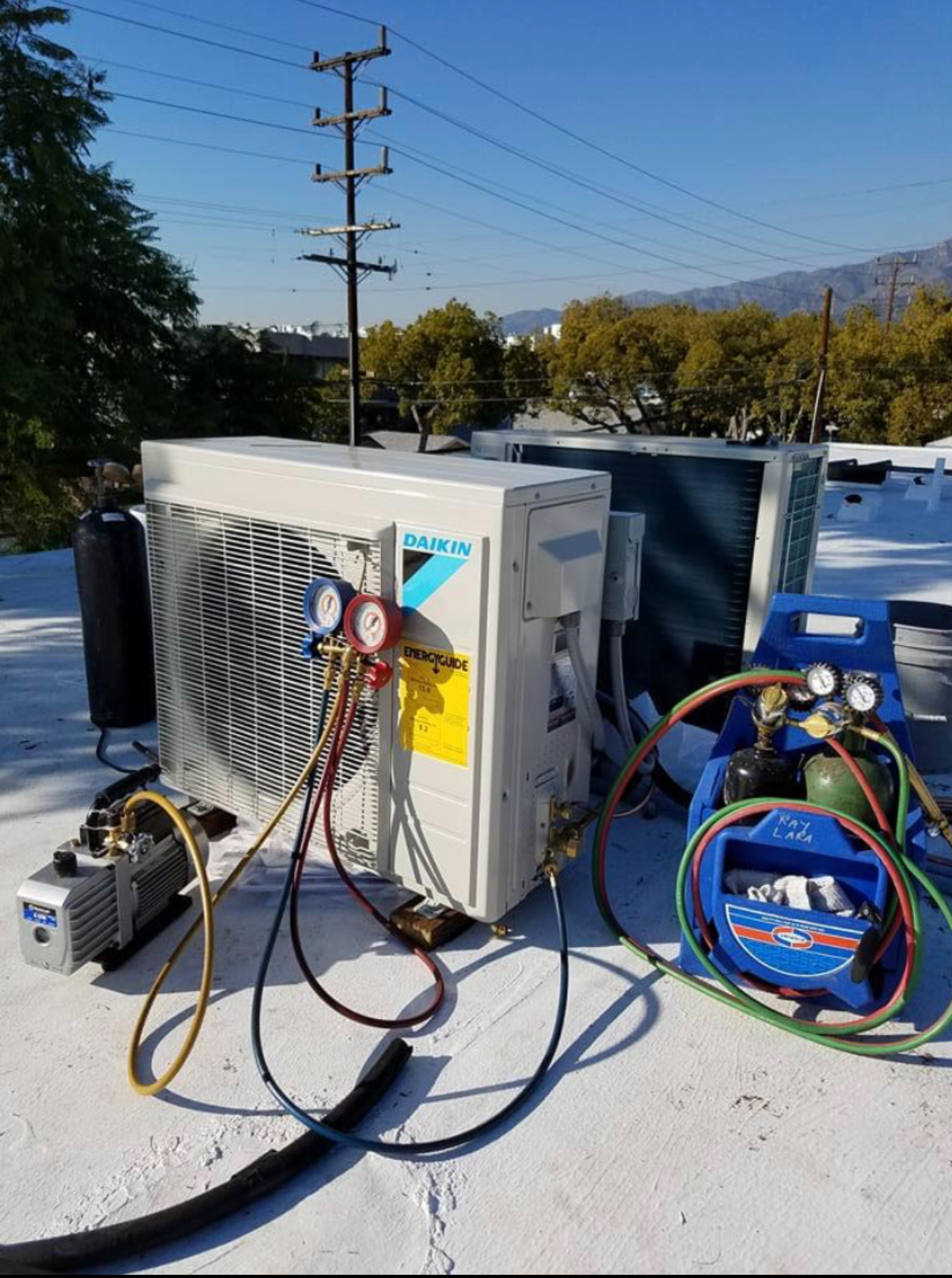 HVAC equipment on a rooftop being serviced with gauges and a vacuum pump.