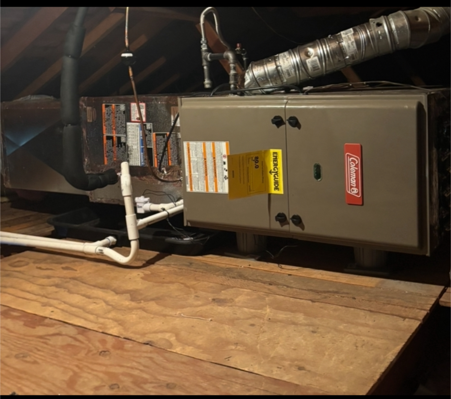 A Coleman furnace in a wood-paneled enclosure with ductwork and gas pipes.