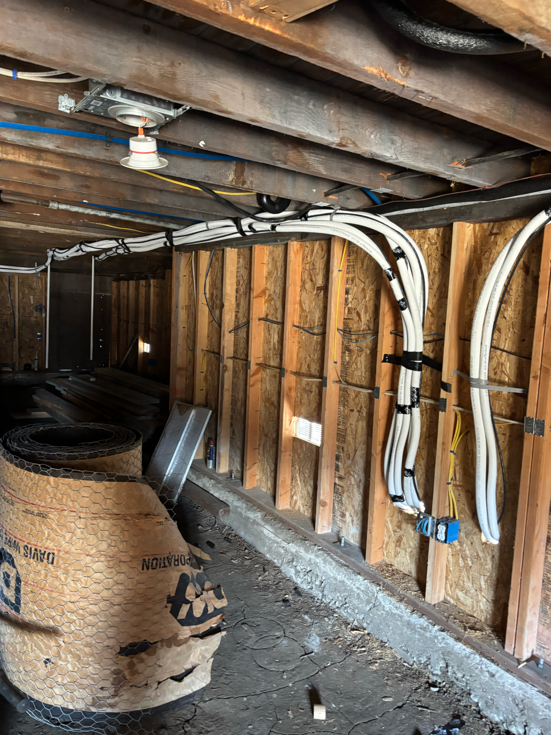 Under-construction interior of a building, showing exposed wooden beams, pipes, and electrical wiring.