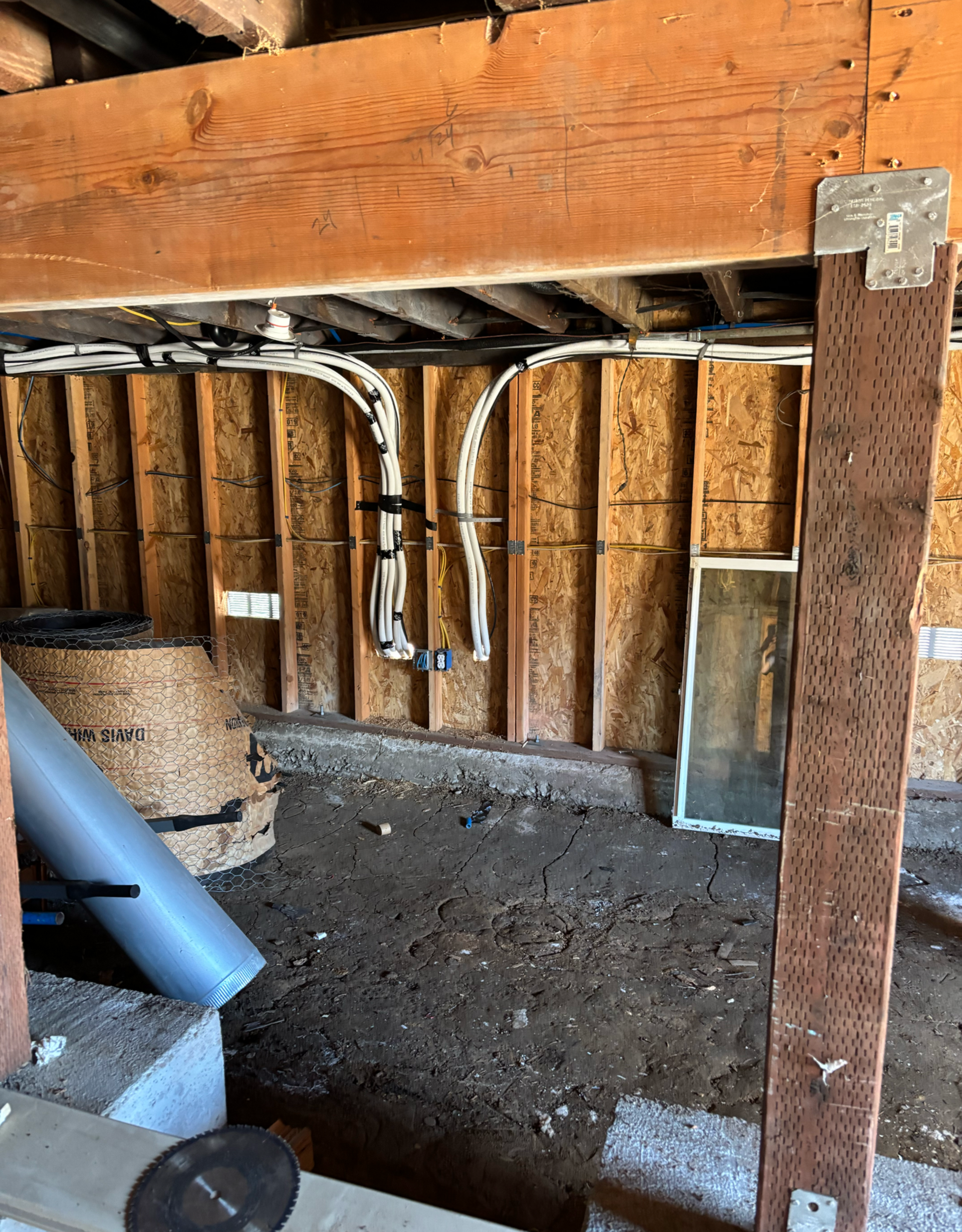 Interior view under wooden structure with wiring, beams, and concrete foundation.