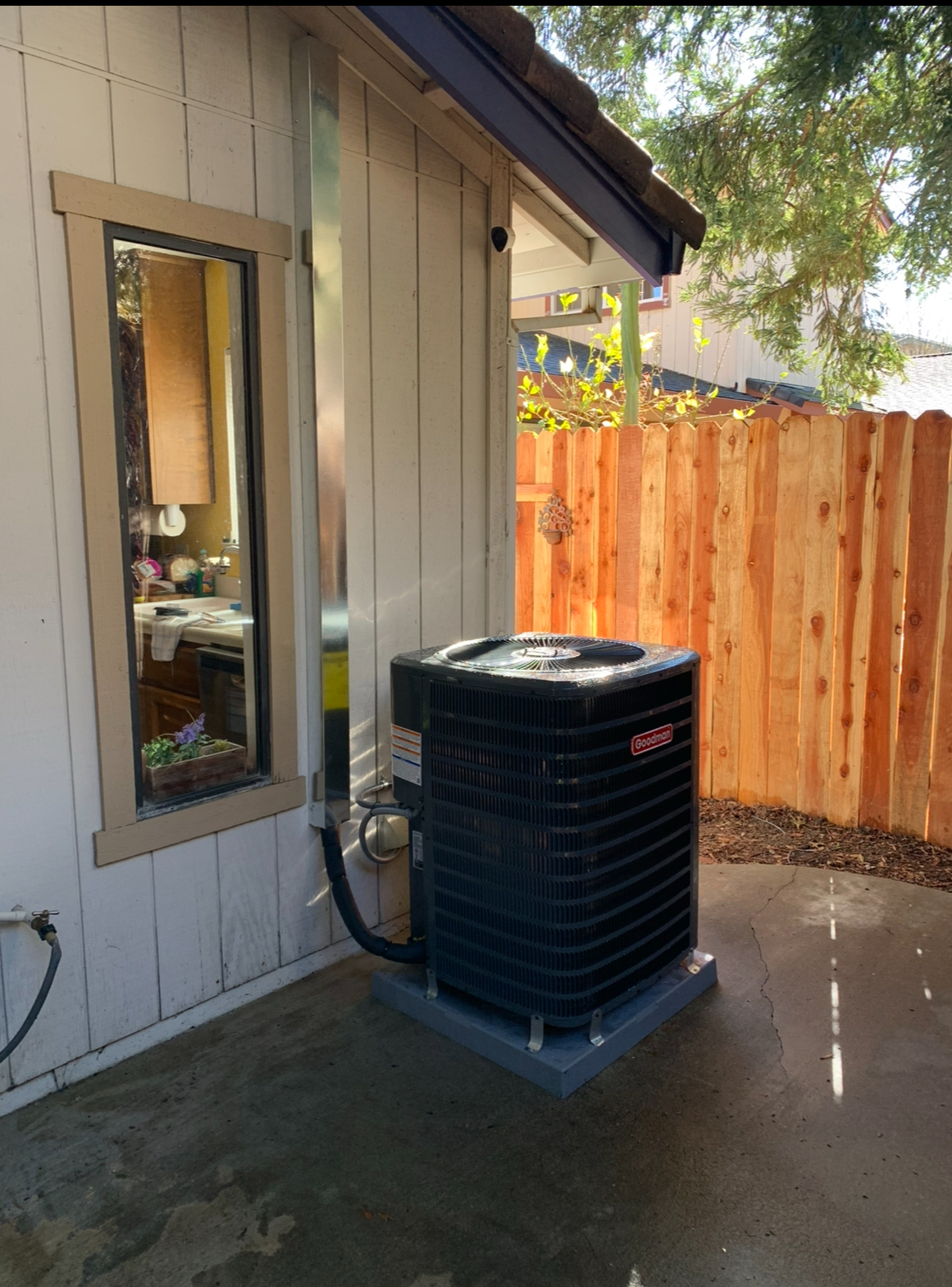 Air conditioner unit next to a window and wooden fence.