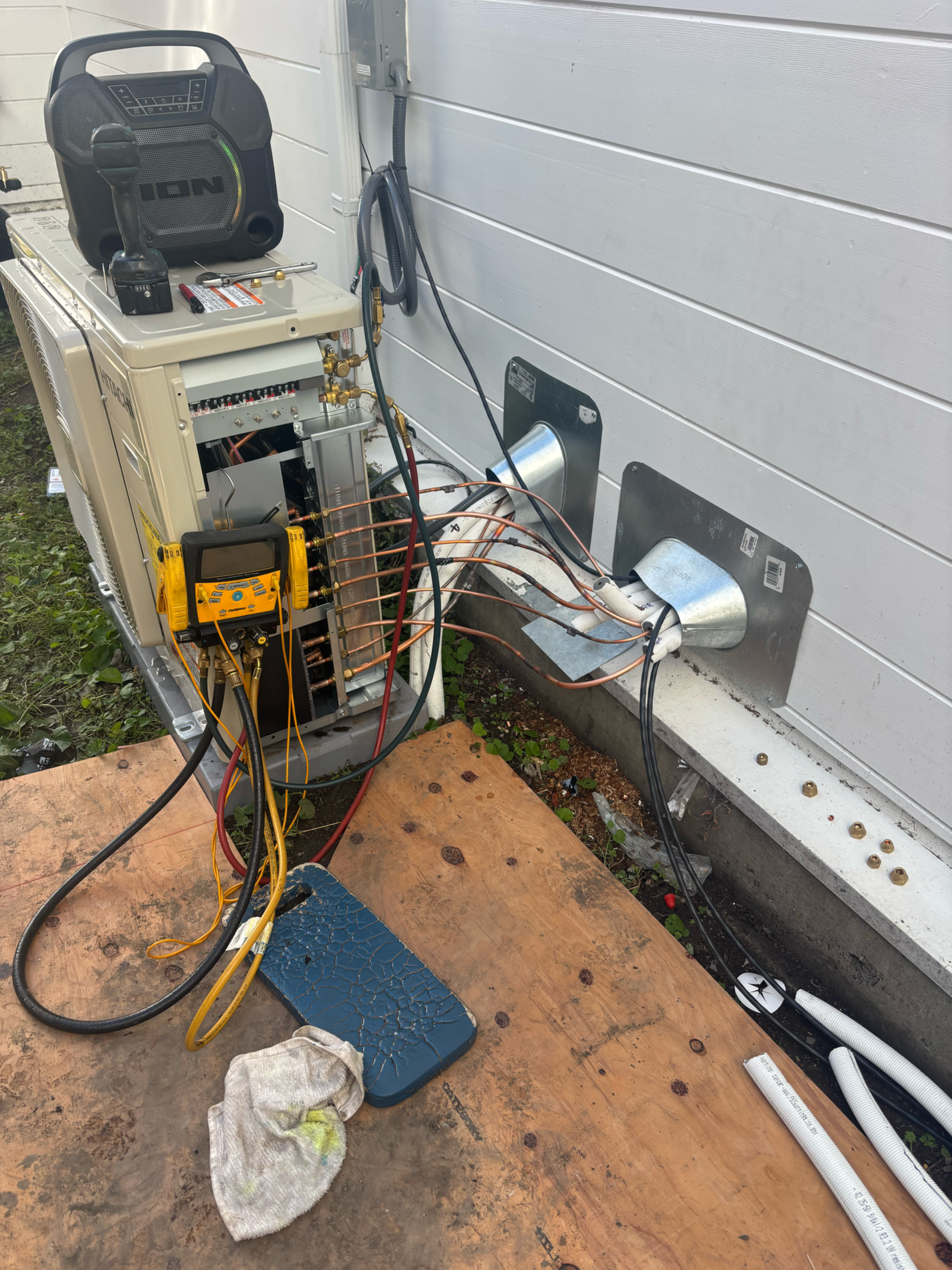 HVAC unit being serviced outdoors, with tools, gauges, and electrical connections visible.