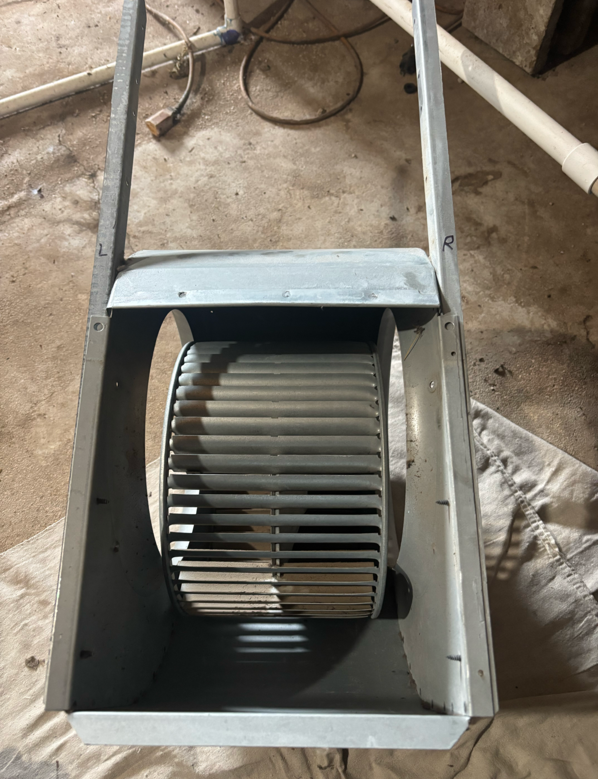 Metal furnace blower fan inside a rectangular housing, on a dirty surface.