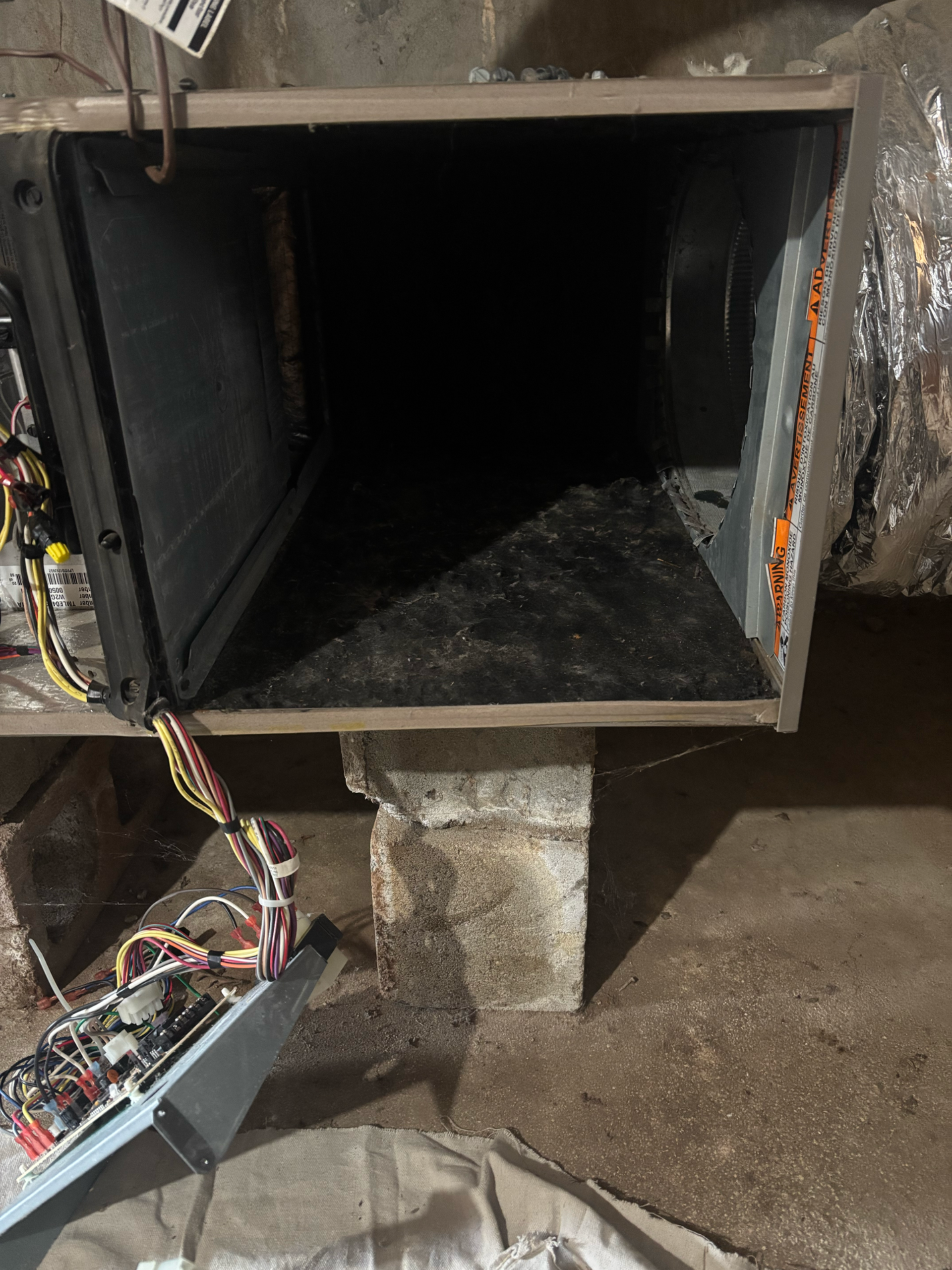 Open furnace ductwork in a dark, damp basement setting. Exposed wiring visible, with insulation.