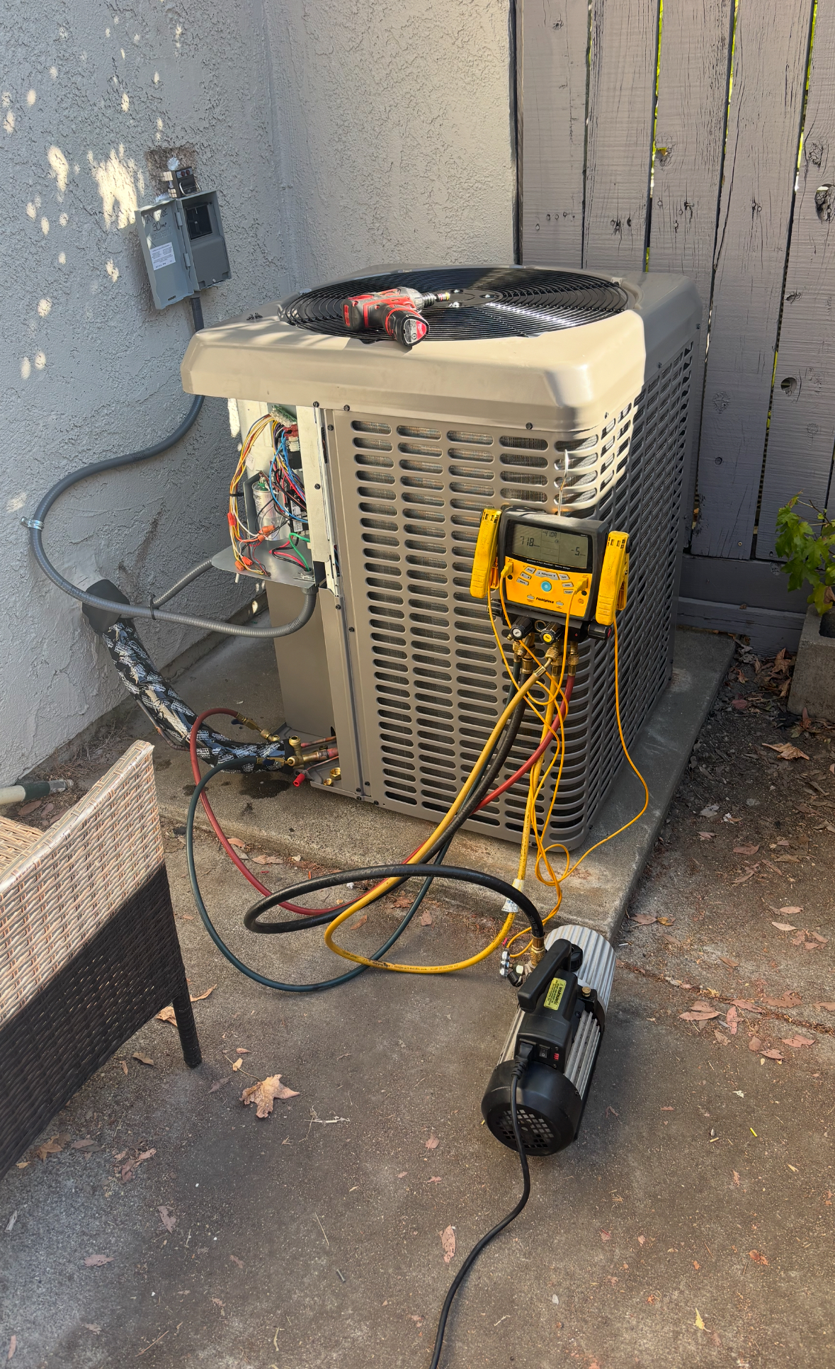 HVAC unit with gauges connected, on concrete patio. Vacuum pump on ground.