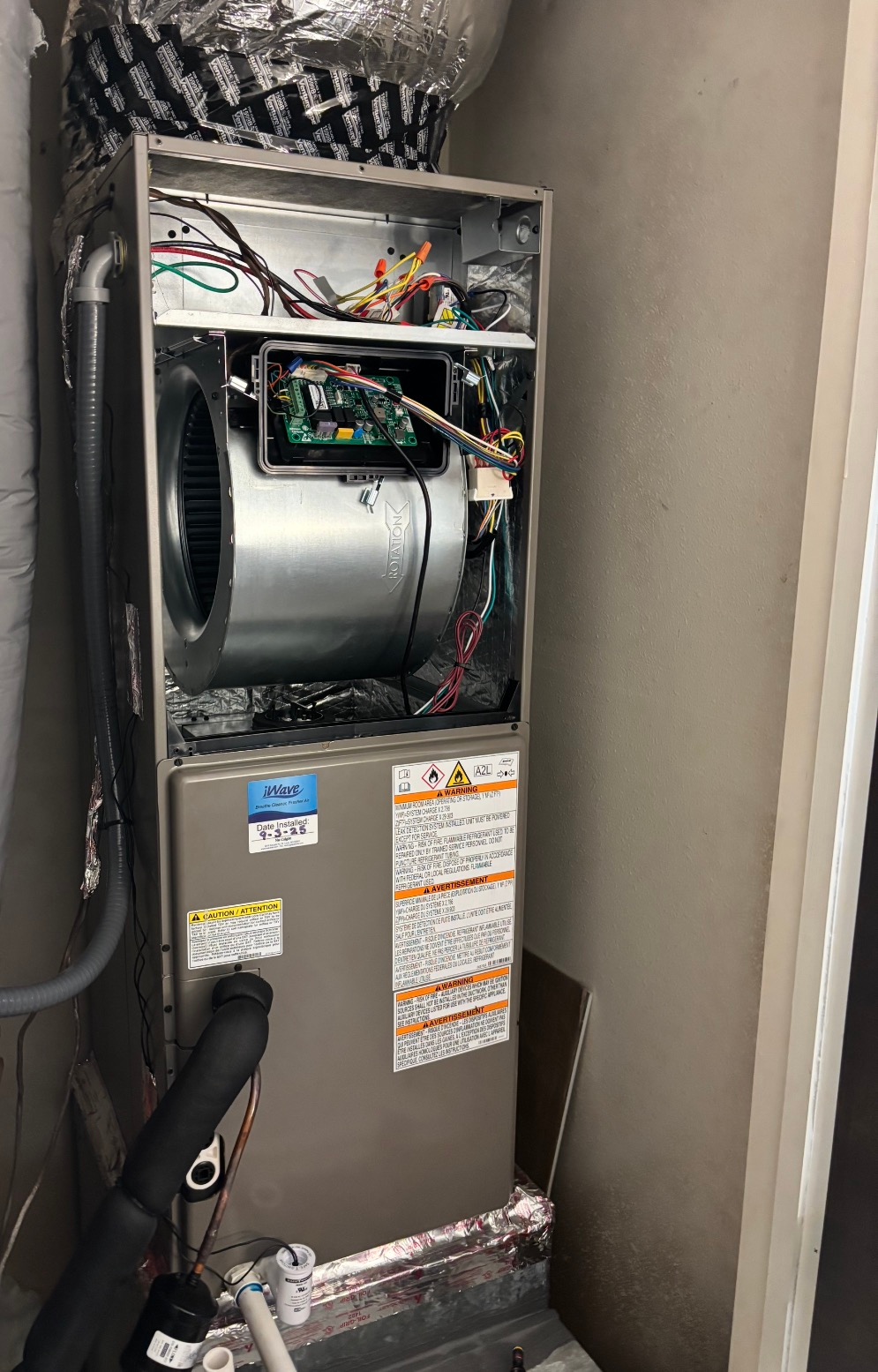 An open furnace unit with exposed wiring, blower, and control panel. Silver metal casing in a utility closet.