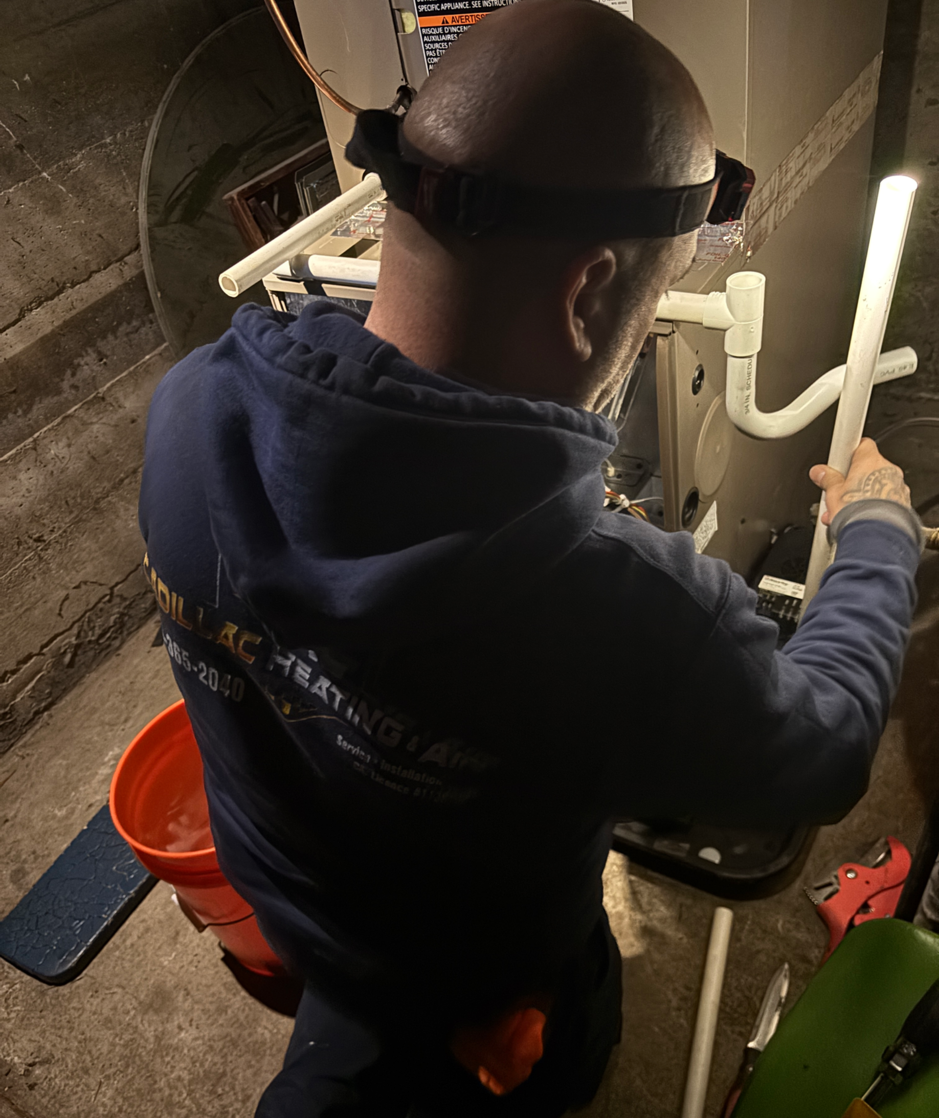 Person working on pipes with a light and headlamp in a basement.