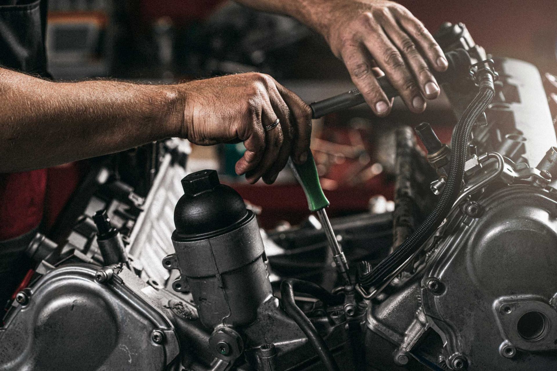 Mechanic working on a car engine with a screwdriver in a garage.