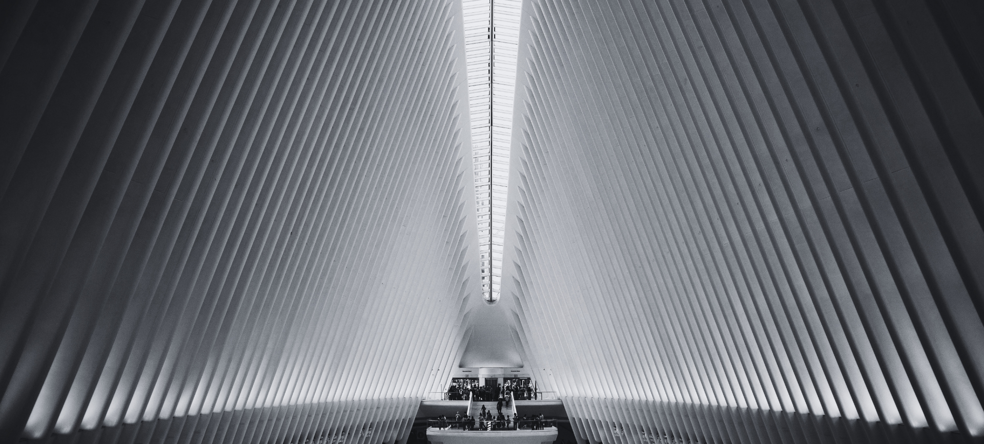 Symmetrical black-and-white hall with tall ribbed walls converging toward a bright central skylight.