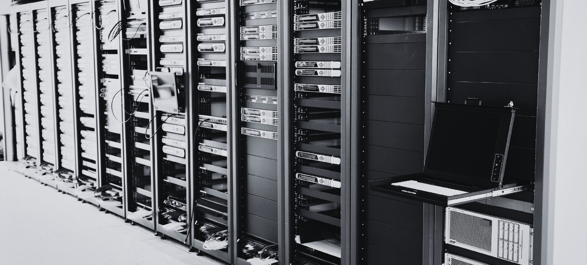 Rows of open server racks in a data center hallway, black equipment in a monochrome setting