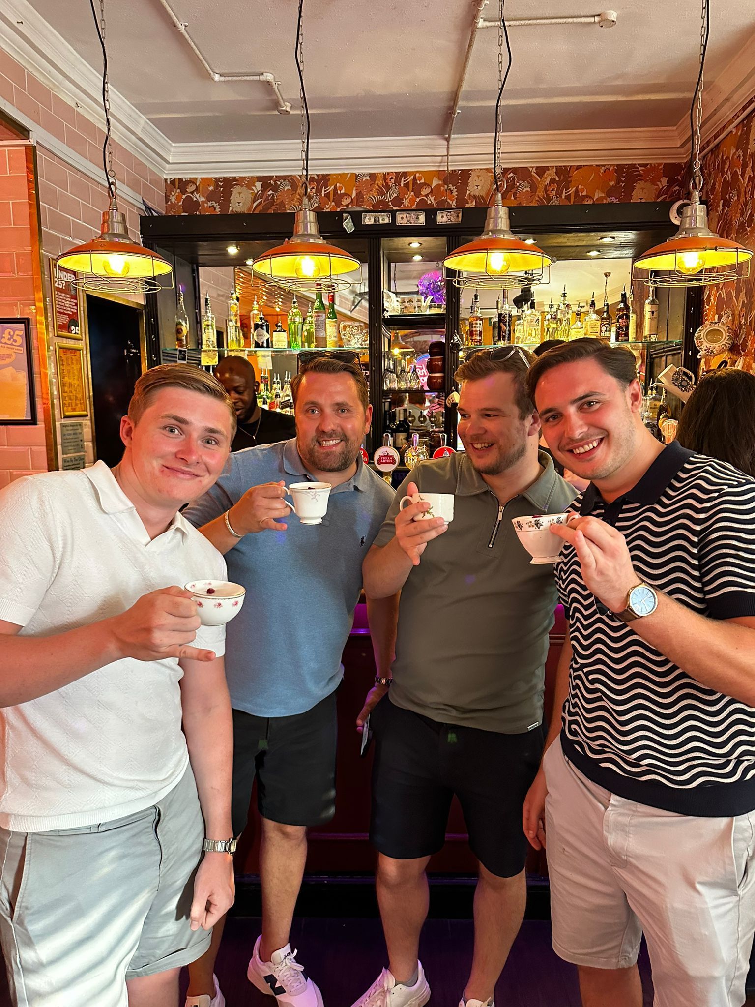Four friends in a cozy bar raise espresso cups and smile at the camera