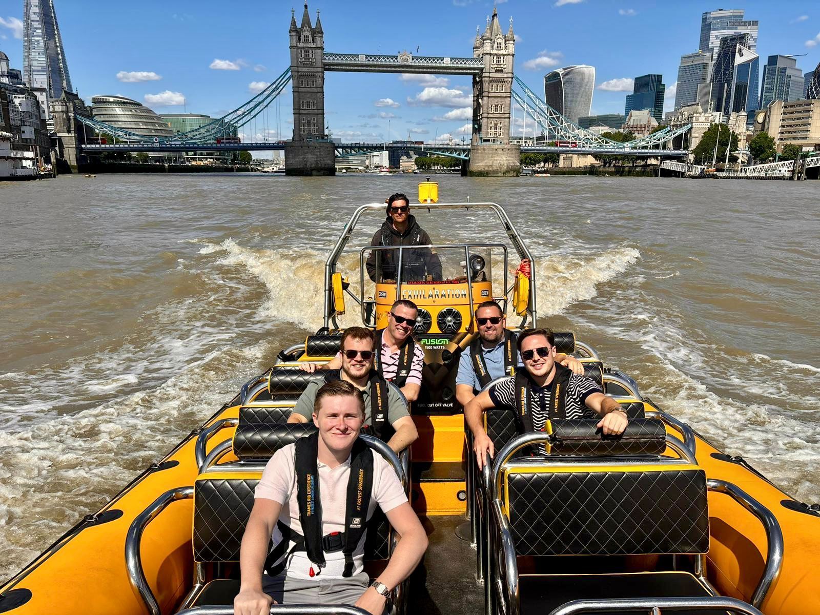 Tourists in a yellow speedboat on the Thames with Tower Bridge and London skyline in the background