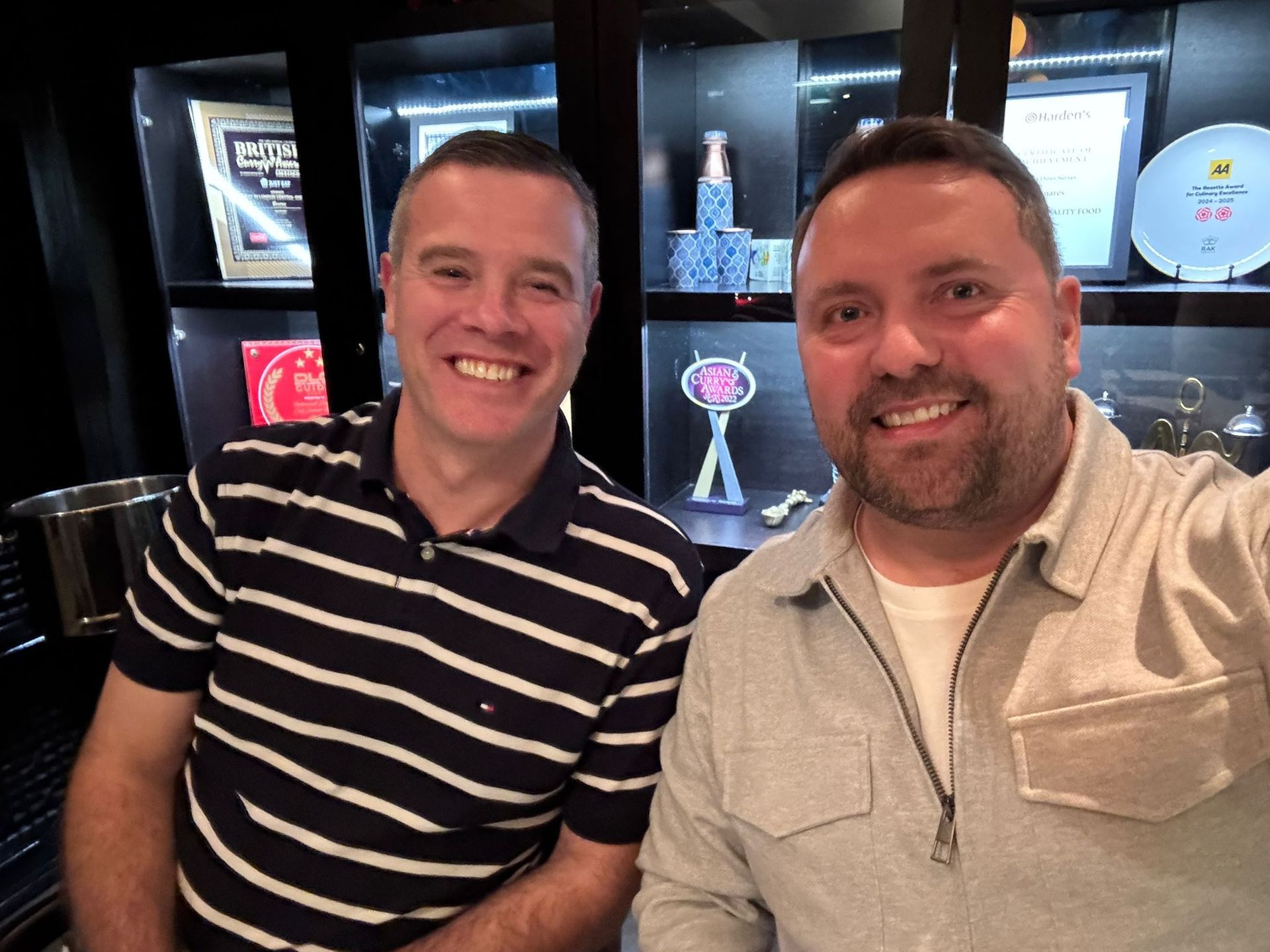 Two smiling men standing indoors in front of illuminated display cases