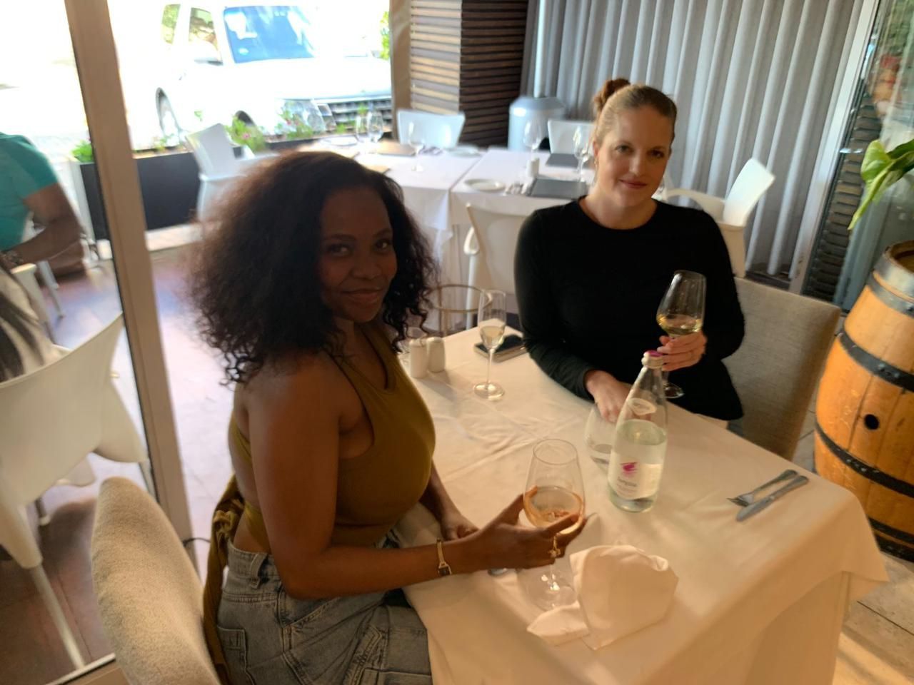 Two women seated at a restaurant table, smiling with drinks and place settings.