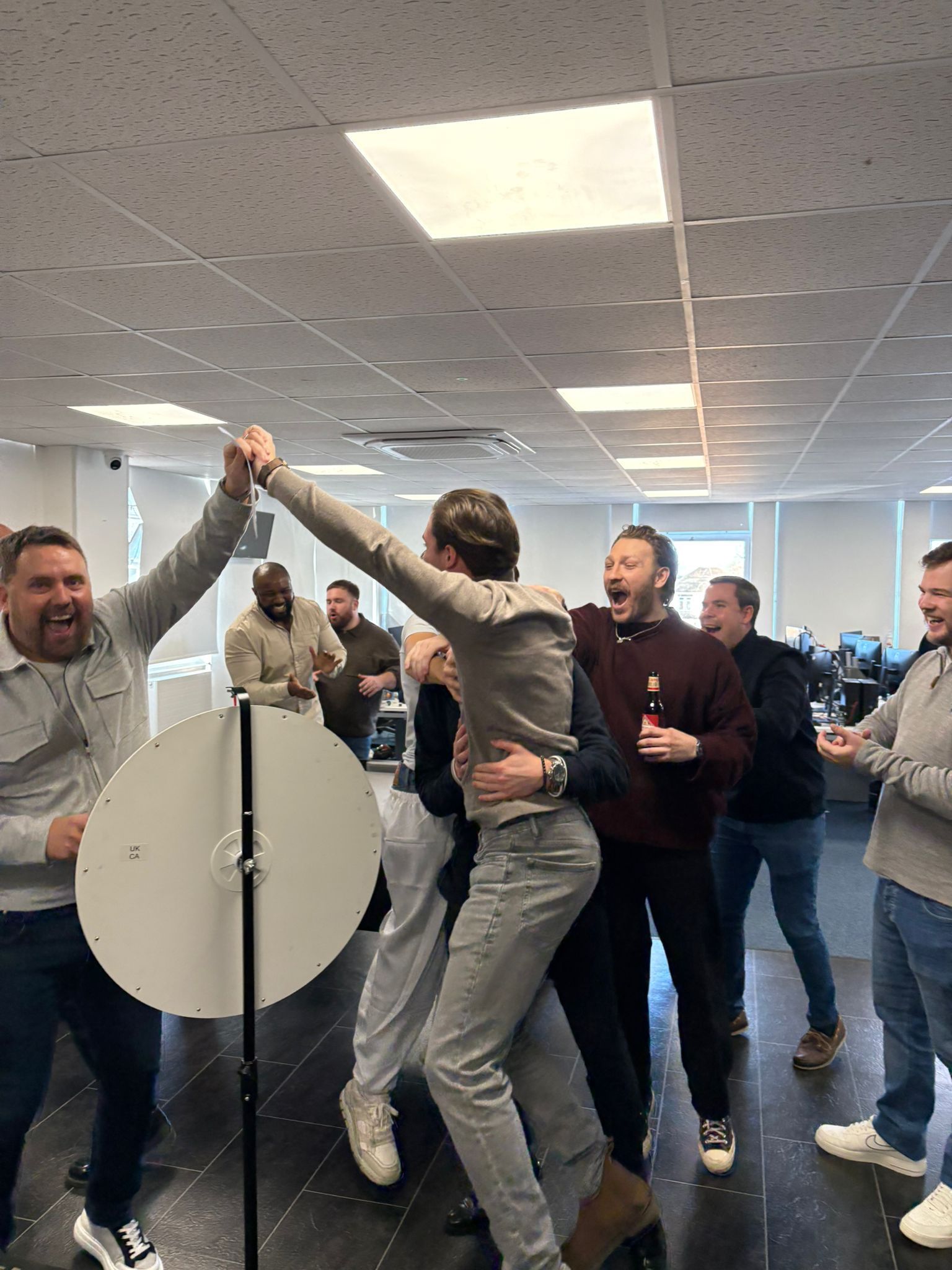 People in an office cheer as two colleagues high-five beside a spinning wheel.