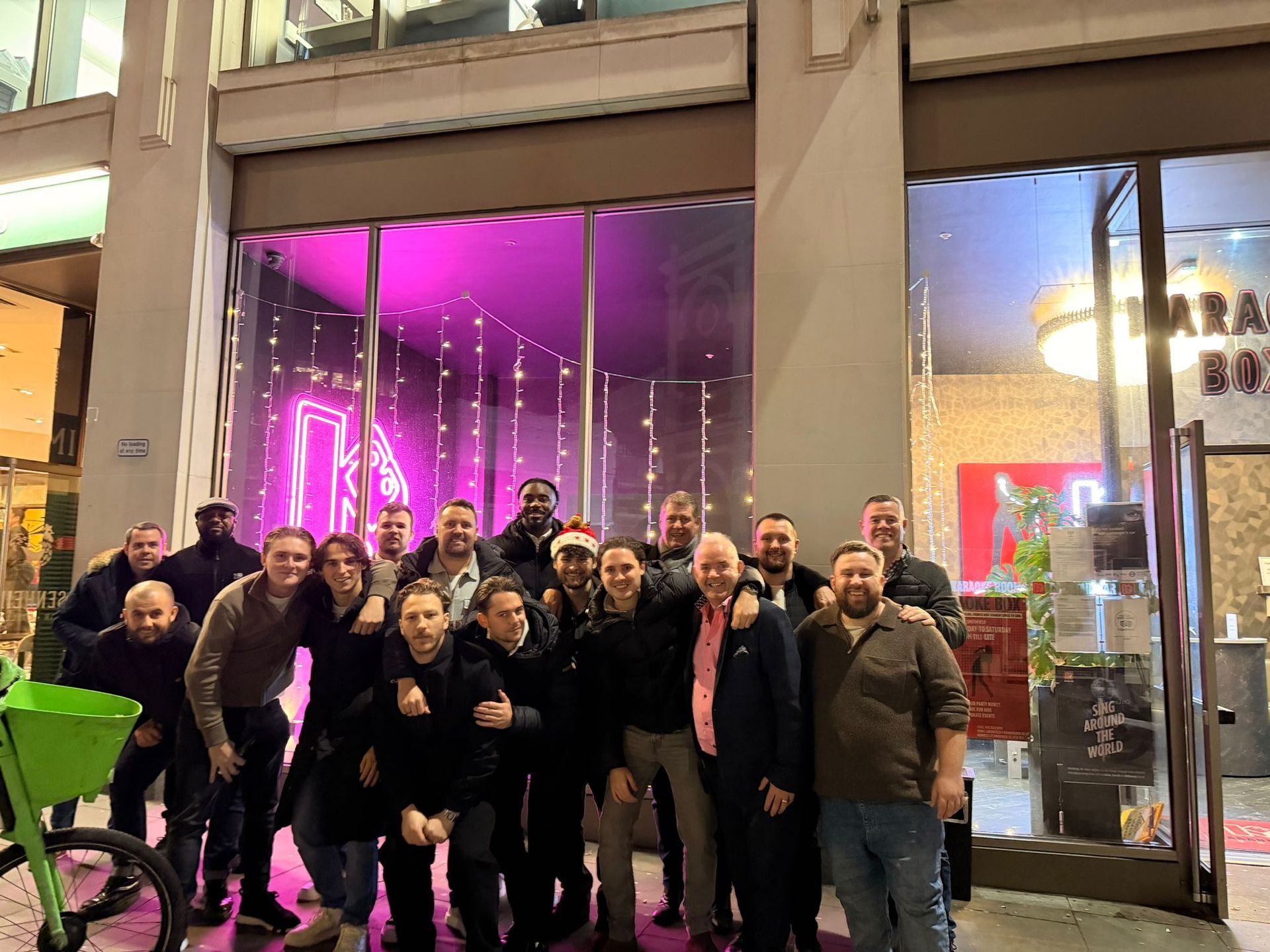 Group of people posing outside a storefront with bright purple neon lights at night