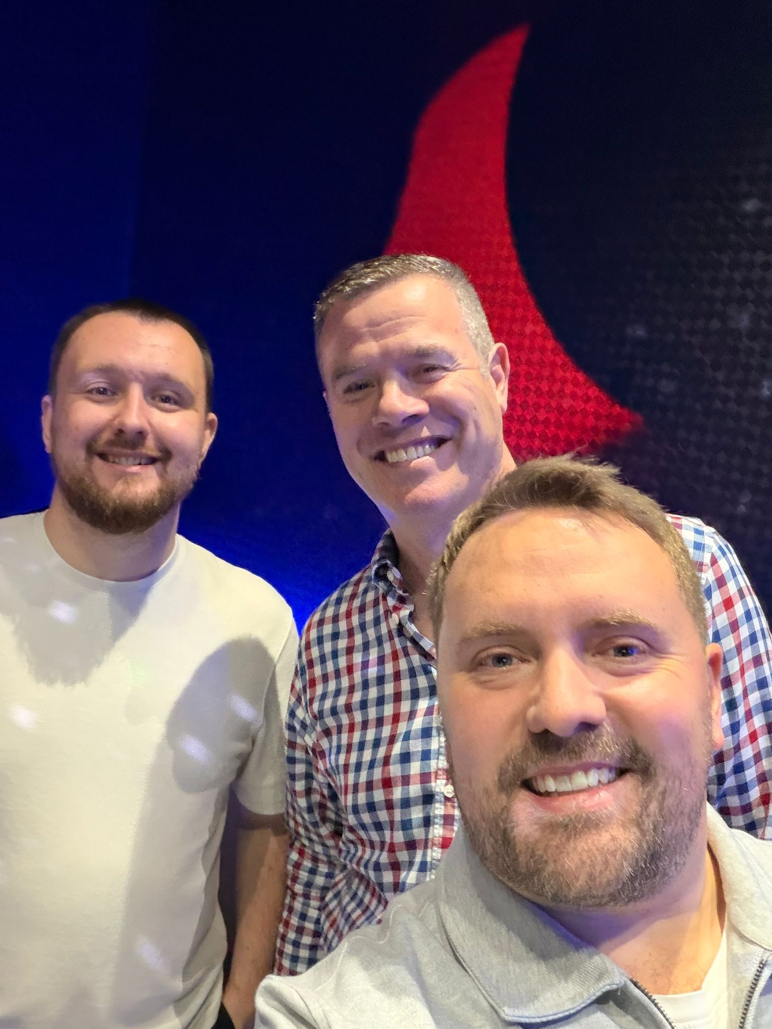 Three smiling people posing indoors in front of a blue and red abstract backdrop