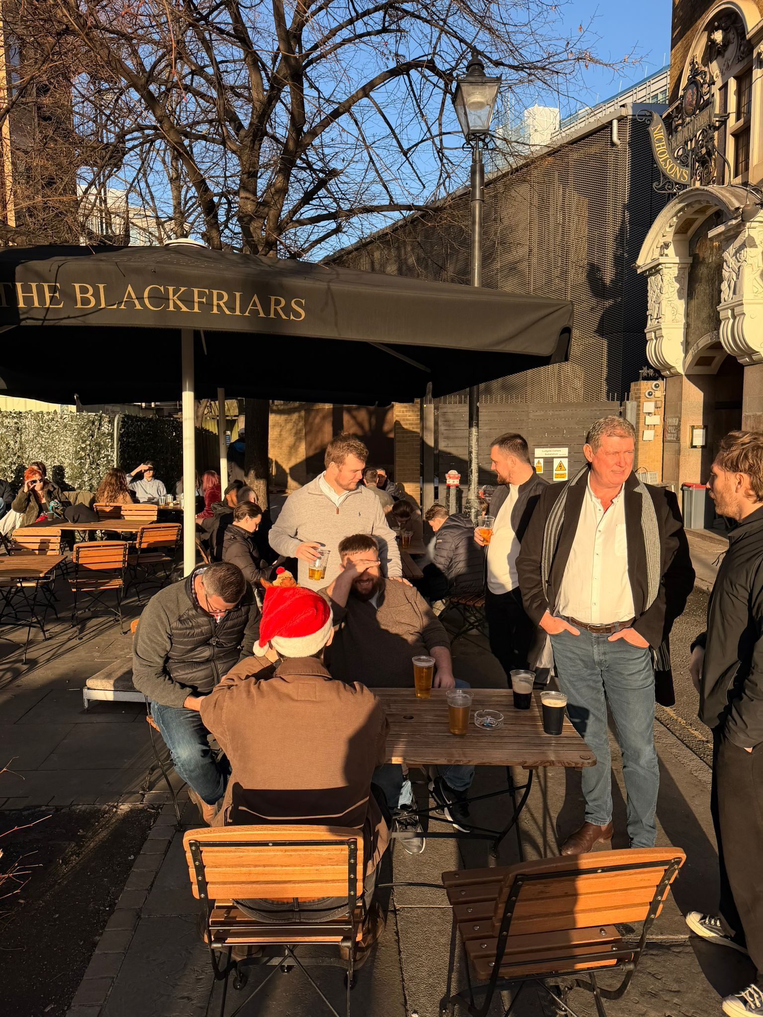 People sitting and standing outside The Blackfriars pub on a sunny day.