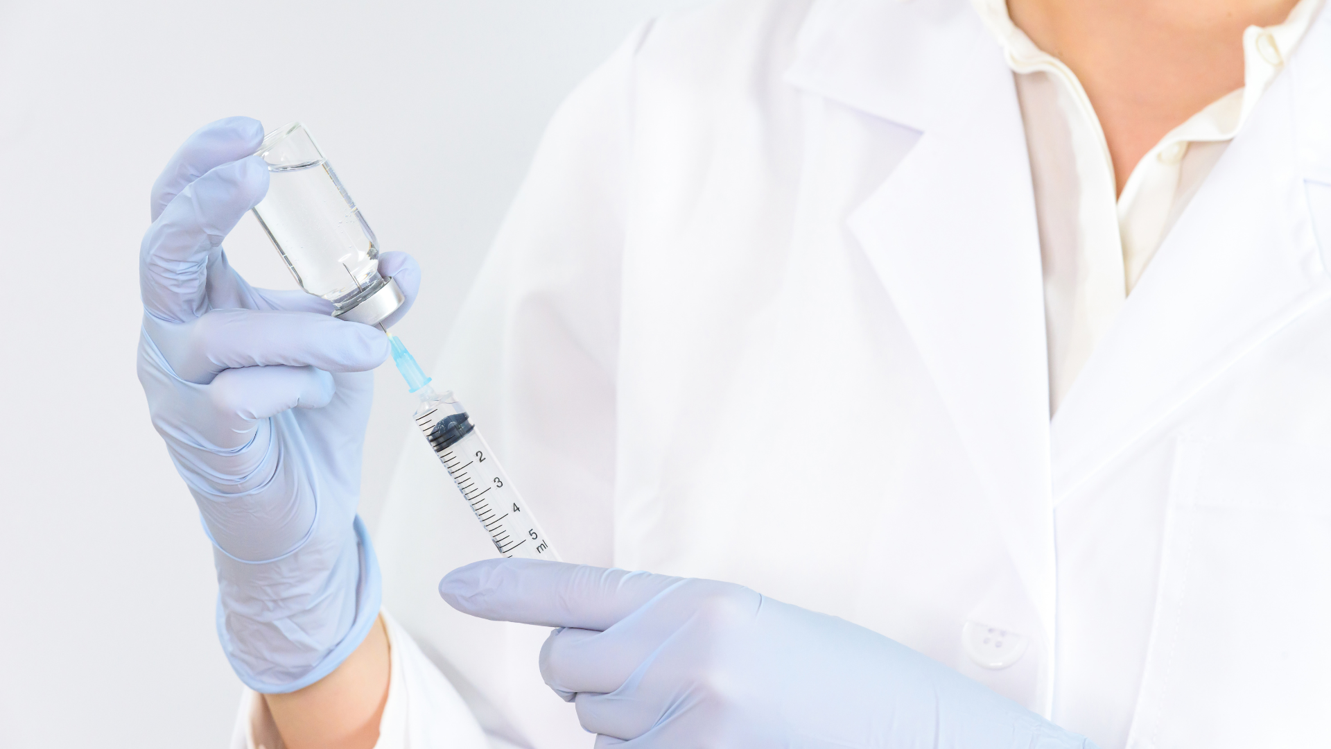 A doctor is holding a syringe and a bottle of liquid.