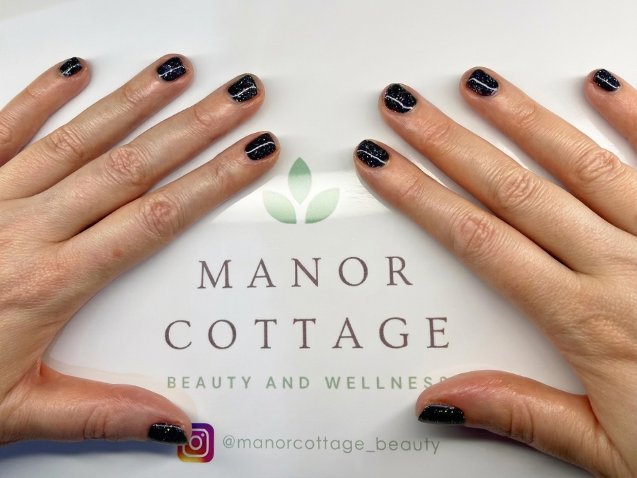 Hands with black nail polish framing Manor Cottage Beauty and Wellness logo on a white background