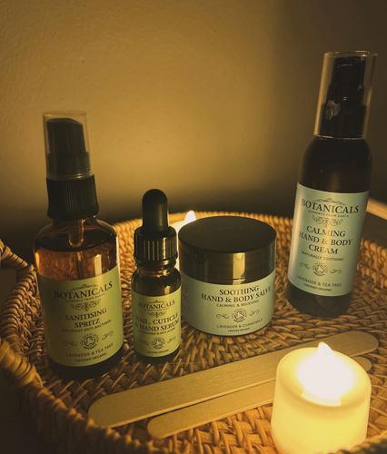 A spa setup with amber bottles, a jar, dropper, wooden sticks, and a lit candle on a woven mat.