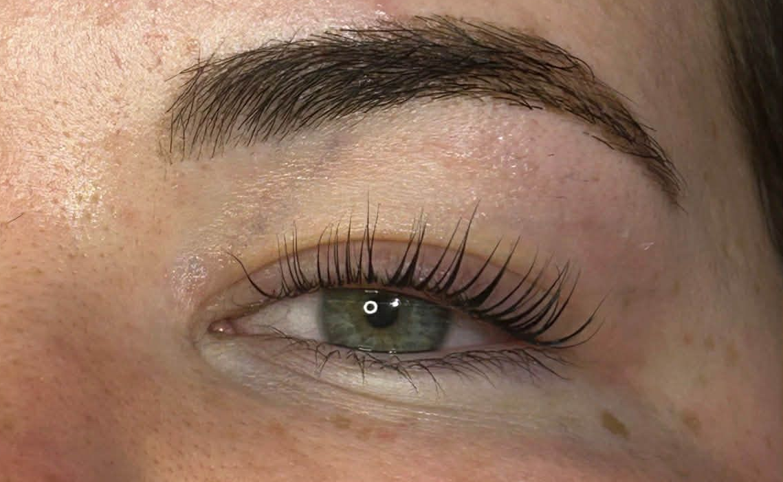 Close-up of a green eye with long eyelashes and shaped eyebrow on fair skin