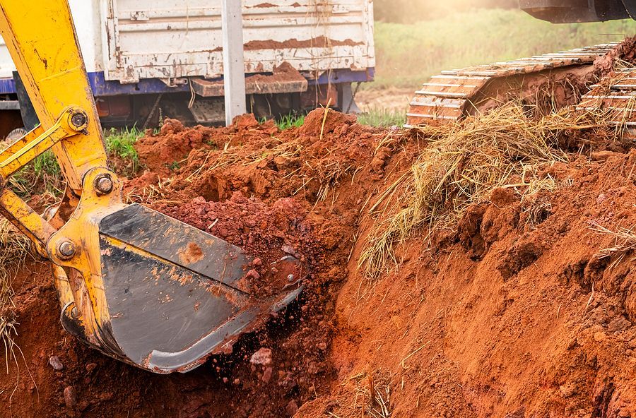 Yellow excavator digging in red soil, creating a trench.