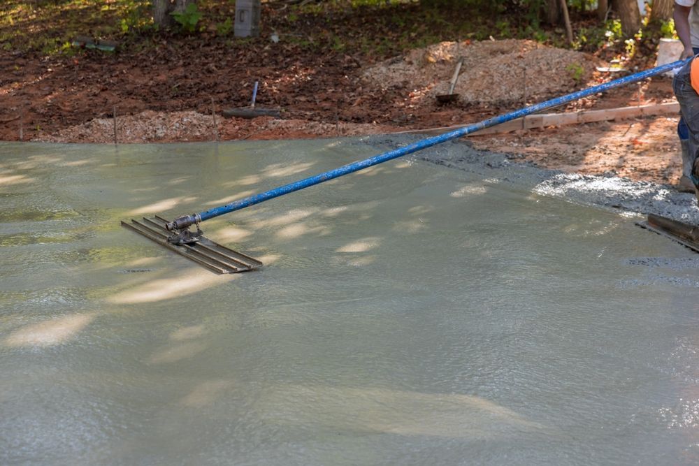 Person smoothing wet concrete with a screed rake outdoors.