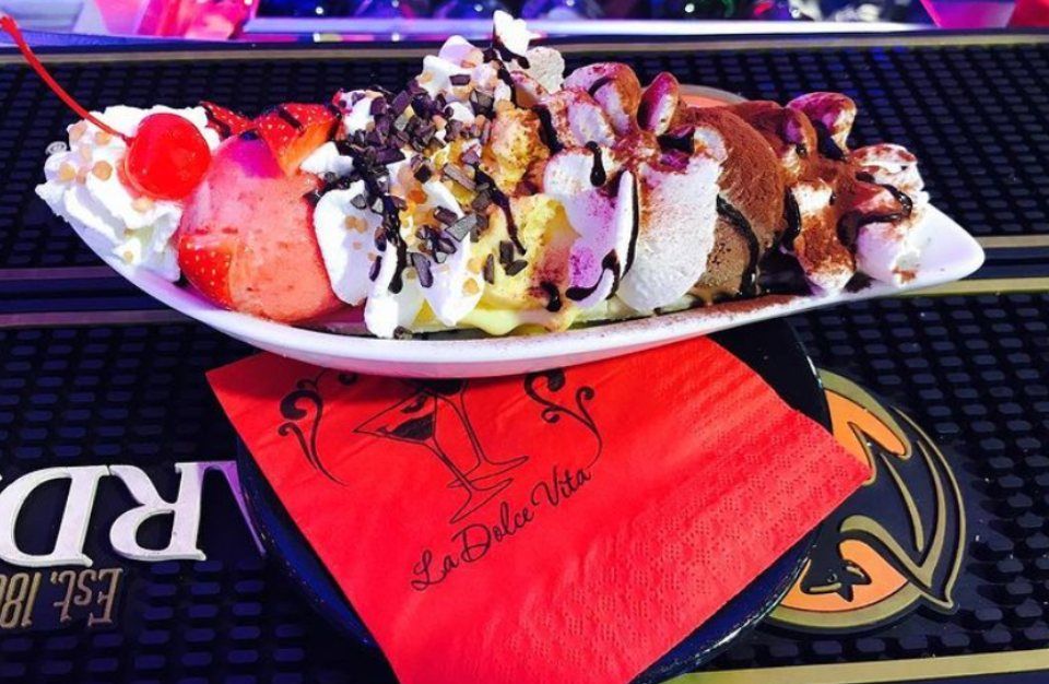 Coppa gelato banana split con panna montata, noci e ciliegia su una barretta.