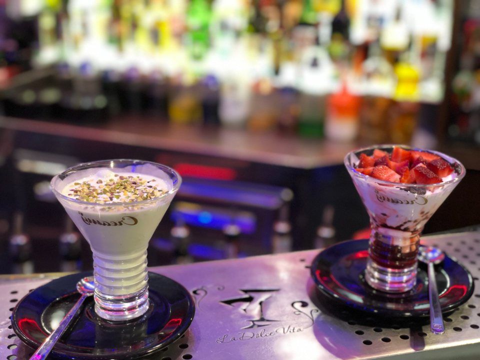 Due cocktail dessert sul bancone di un bar. Uno guarnito con granella di zucchero, l'altro con fragole.