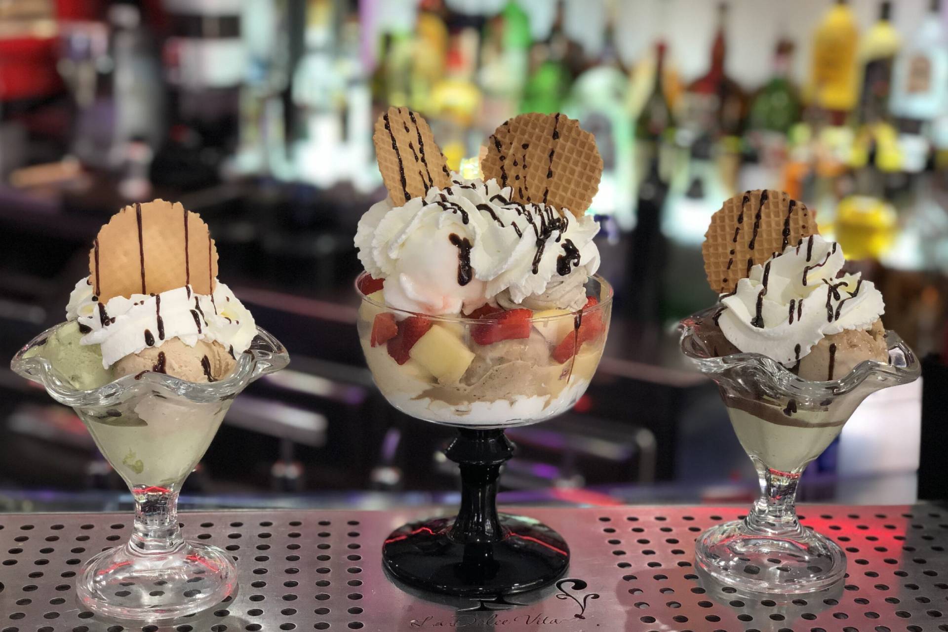 Tre elaborate coppe gelato con biscotti e panna montata, su un bancone.