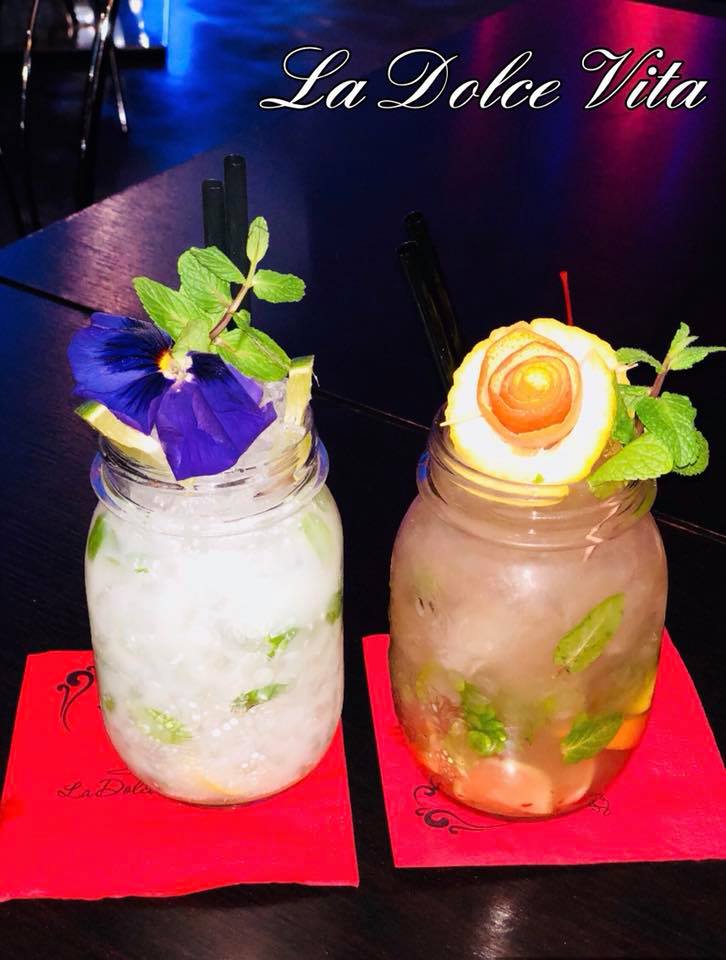 Due cocktail in barattoli di vetro guarniti con erbe aromatiche e agrumi, serviti su tovaglioli rossi.