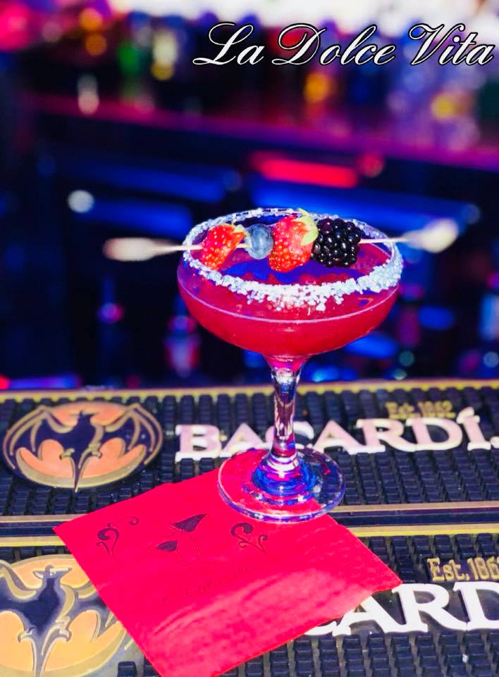 Cocktail rosso con bordo di zucchero, bacche su uno spiedino, servito su un bancone con il logo Bacardi e un tovagliolo rosso.