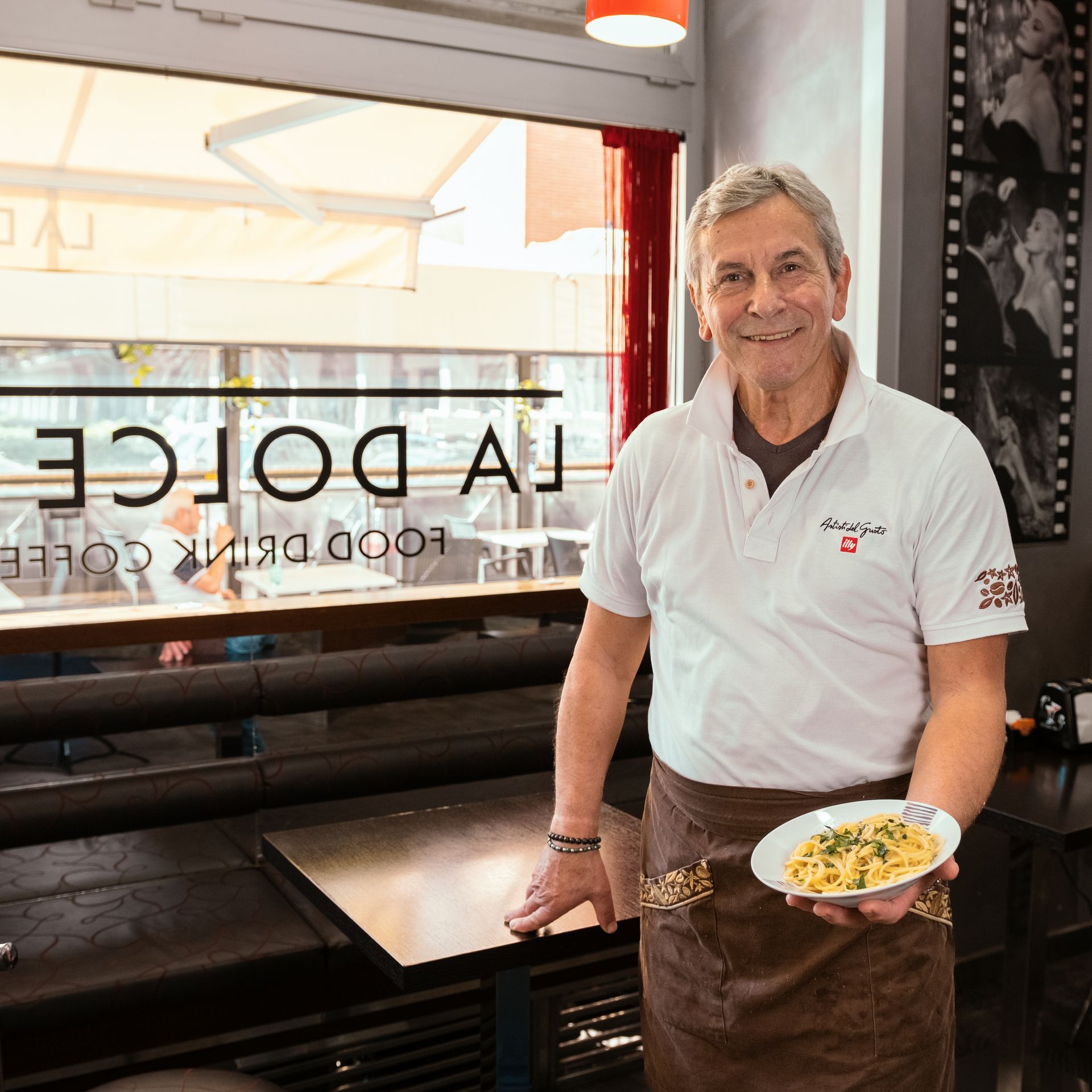Un uomo in camicia bianca tiene in mano un piatto di pasta, in piedi nel bar